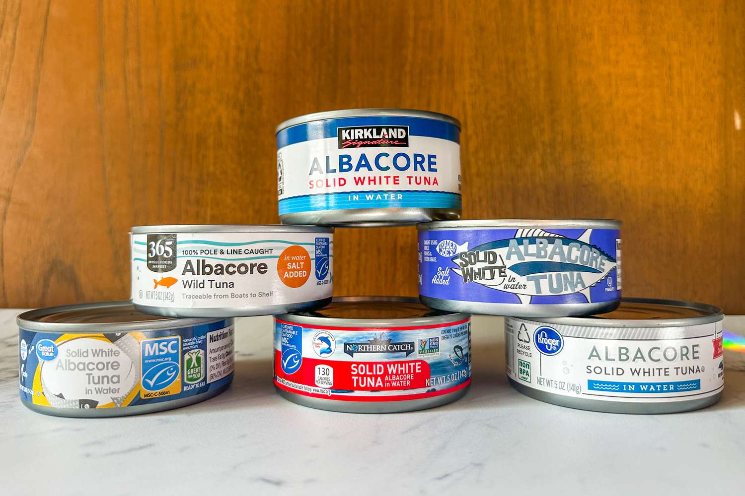 A variety of canned tuna brands displayed on a white surface, arranged in a small pyramid formation