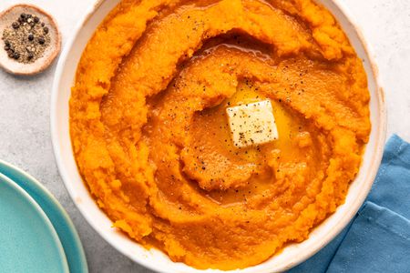 Overhead view of a white bowl of butternut squash topped with butter ad spices resting on a blue table napkin