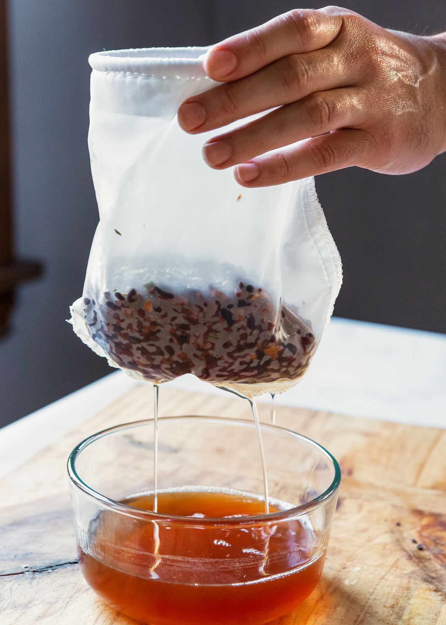 A bag of ingredients for cocktail bitters lifted out of a glass bowl.