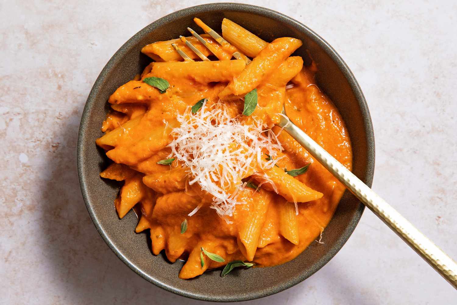 Ina Garten's penne alla vodka in a brown bowl with a fork, sprinkled with Parmesan