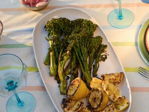 Platter of grilled broccolini and lemon slices on a table set with dishes and glasses