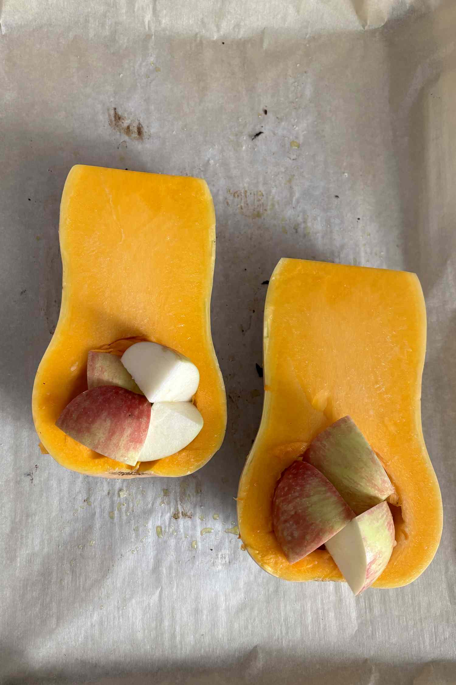 Halved butternut squash with pieces of apple and garlic placed in the cavities