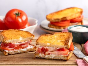 Sliced tomato sandwich on toasted bread with spread on a wooden surface