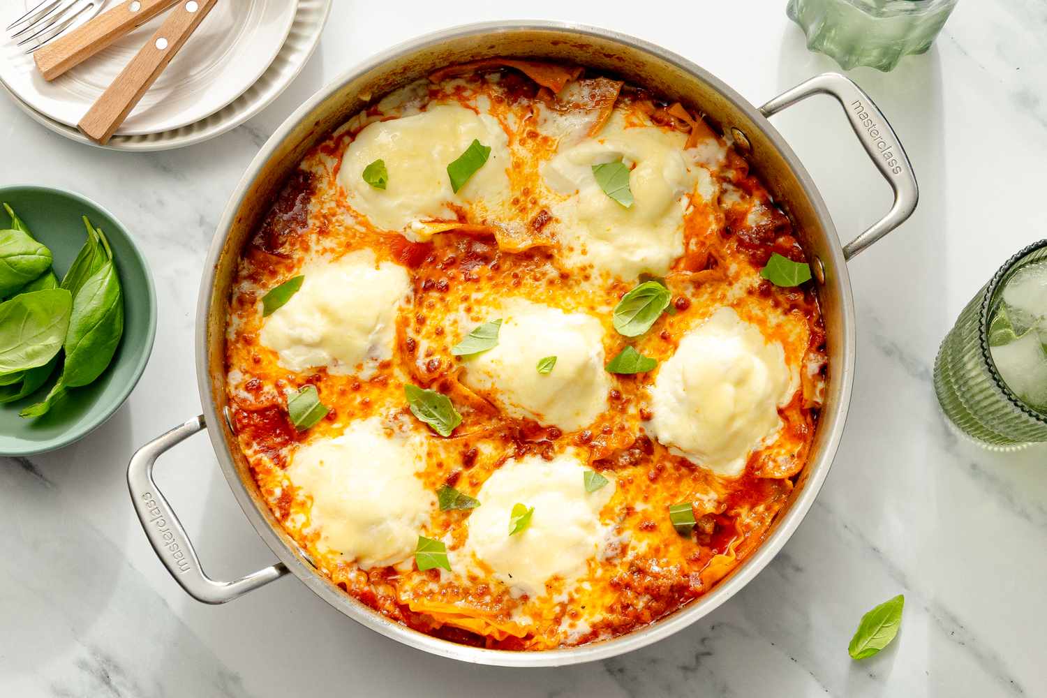 A skillet containing a freshly cooked lasagna topped with dollops of ricotta cheese and garnished with basil leaves