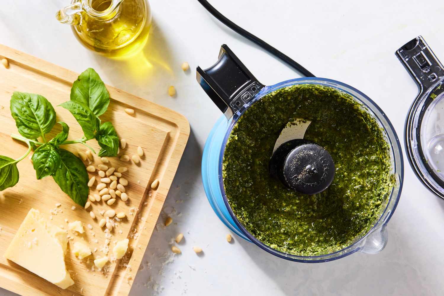 Food processor with basil pesto wooden board with basil cheese and pine nuts nearby