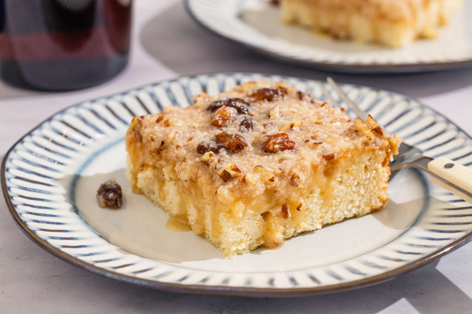 A square slice of cake with a topping containing raisins and nuts on a decorative plate