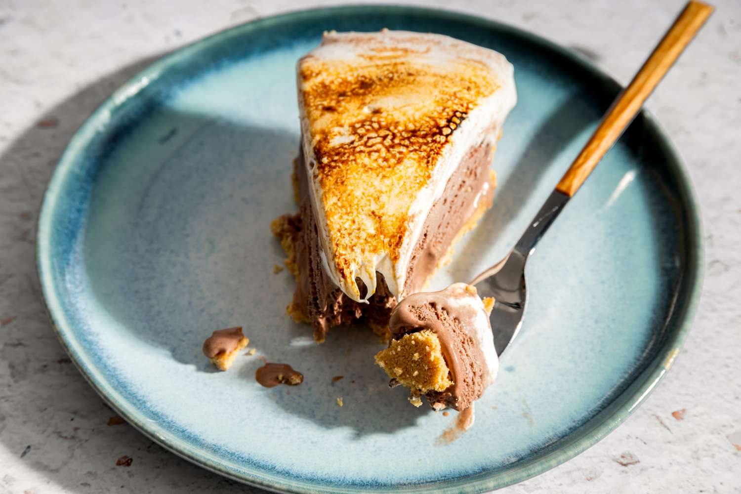 A slice of frozen smores pie served on a plate topped with toasted marshmallow and a fork on the side
