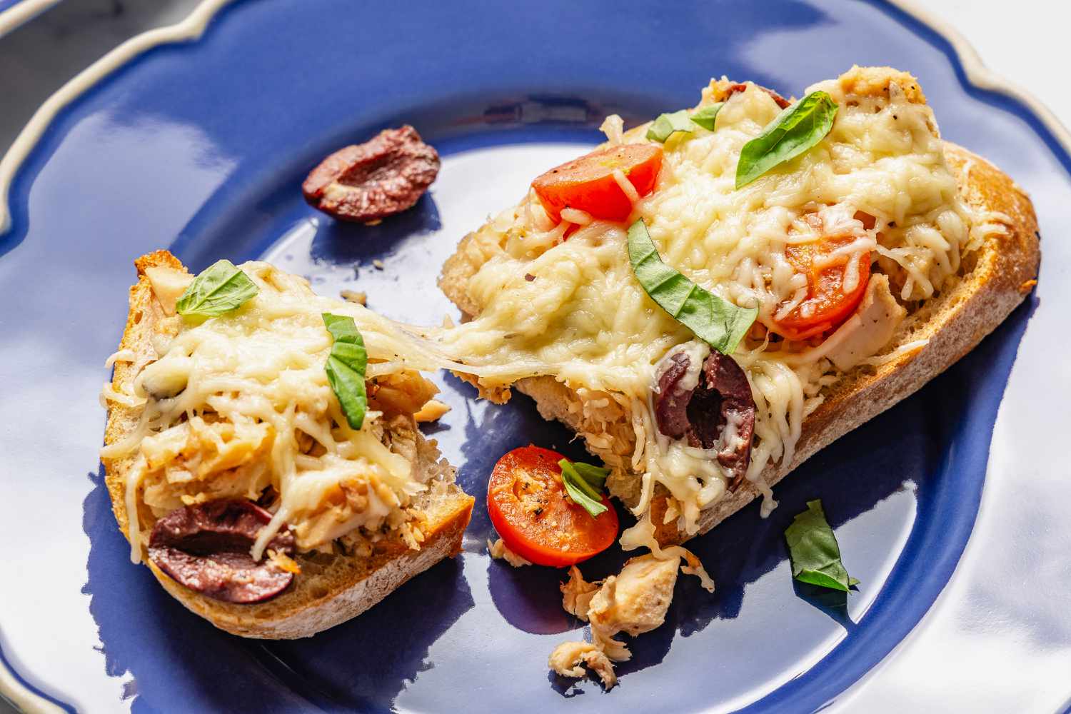 a plate with a Tuna Niçoise Melt torn in half with a nice cheese pull