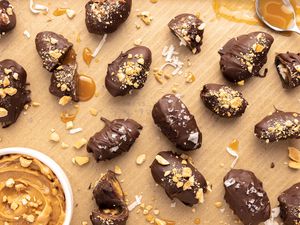 Candy Bar Dates Surrounded by Crushed Peanuts, Coconut Slivers, Caramel Sauce, and a Bowl of Peanut Butter