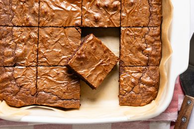 Overhead view of a white baking dish of 3-ingredient brownies on parchment paper, sliced into squares with one slice removed