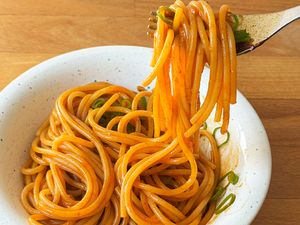 A bowl of cooked noodles being lifted by a fork garnished with green onion slices
