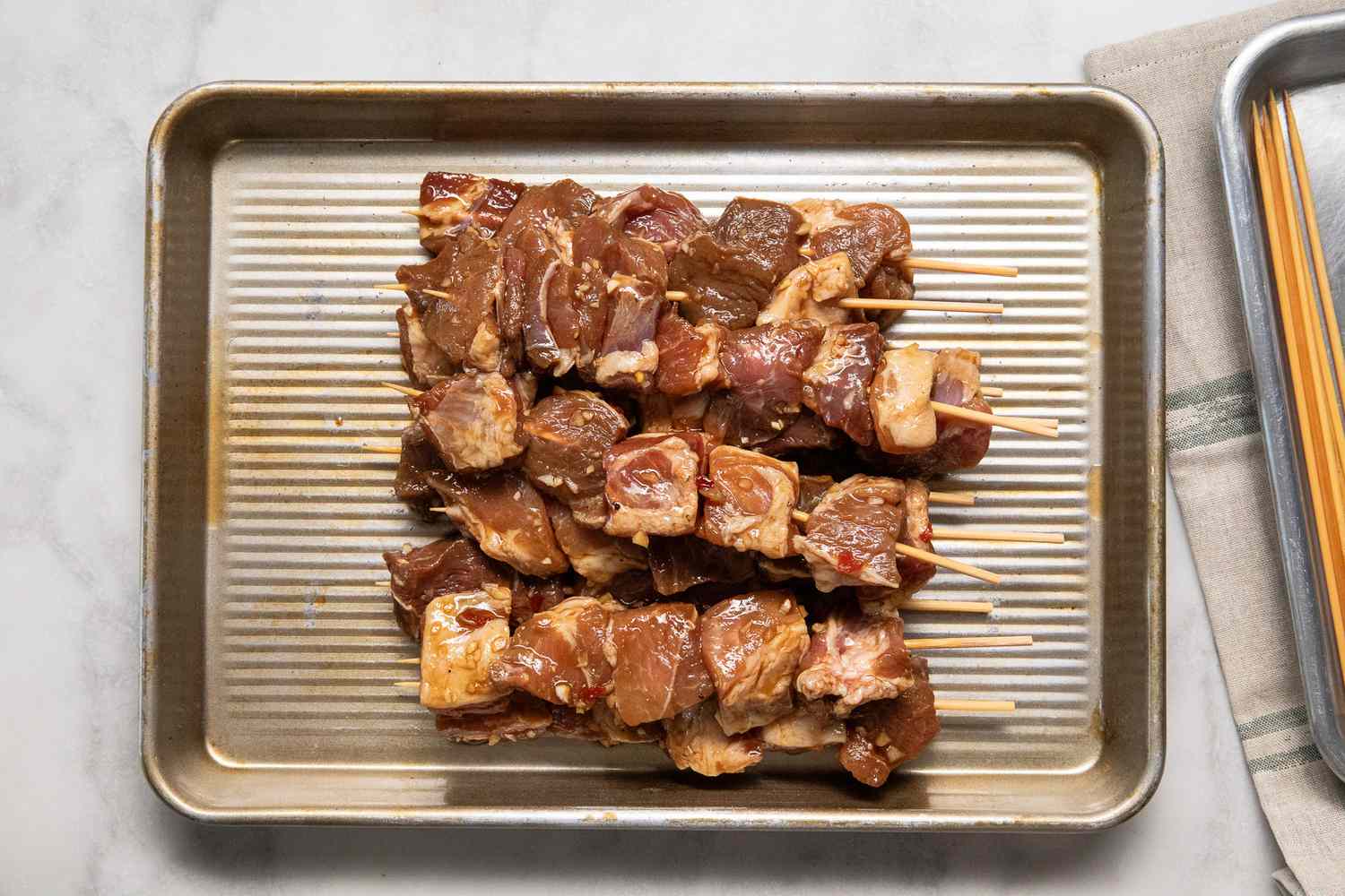 marinated pork on wooden skewers sitting on a baking sheet