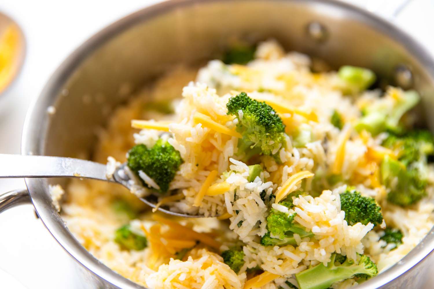 A pot of broccoli and cheese mixed with rice closeup view with a serving spoon
