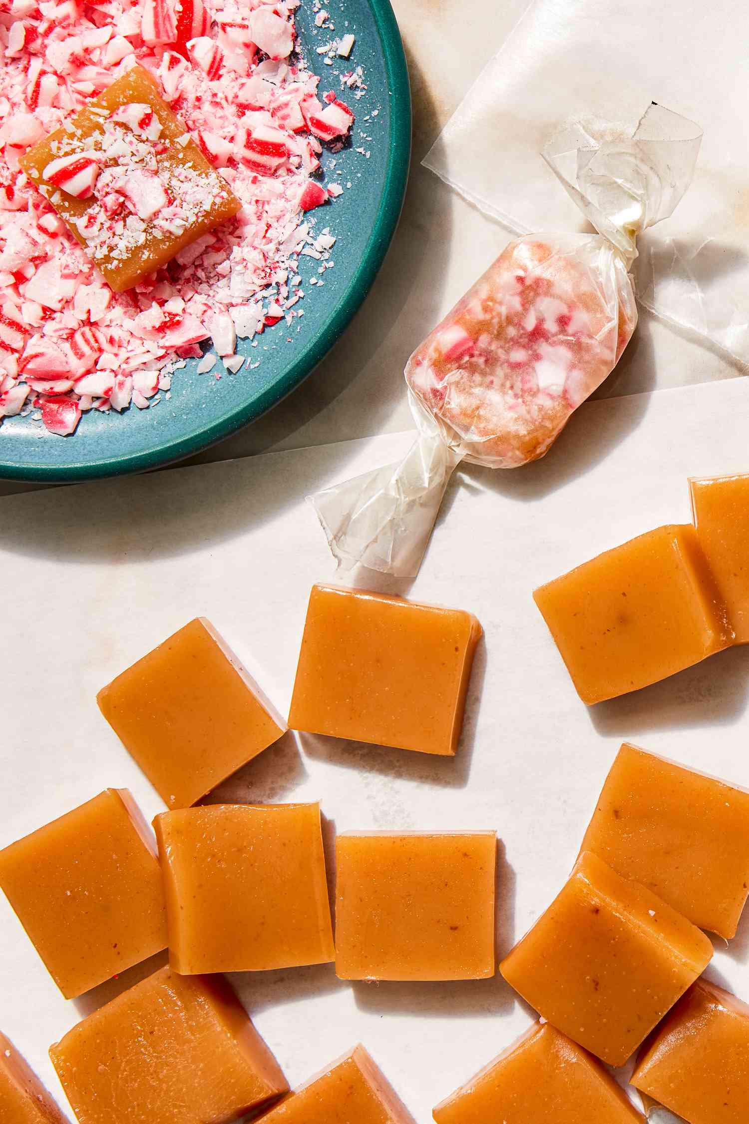 Peppermint Caramels with One Wrapped in Wax Paper, One in a Bowl Small Bowl of and Topped with Crushed Candy Cane, and Some on the Counter Without Toppings