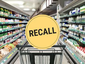 Supermarket aisle with a shopping cart in the foreground and a recall warning sign displayed prominently