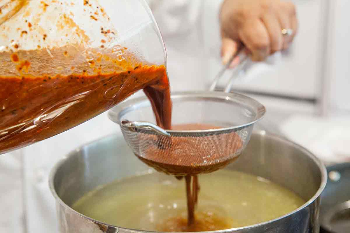 Red pozole sauce being strained into pot 