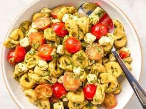A bowl of tortellini salad with pesto, cherry tomatoes, and mozzarella