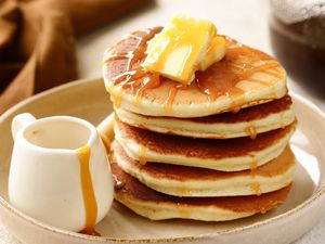 Stack of pancakes with butter and syrup served with a small jug of syrup