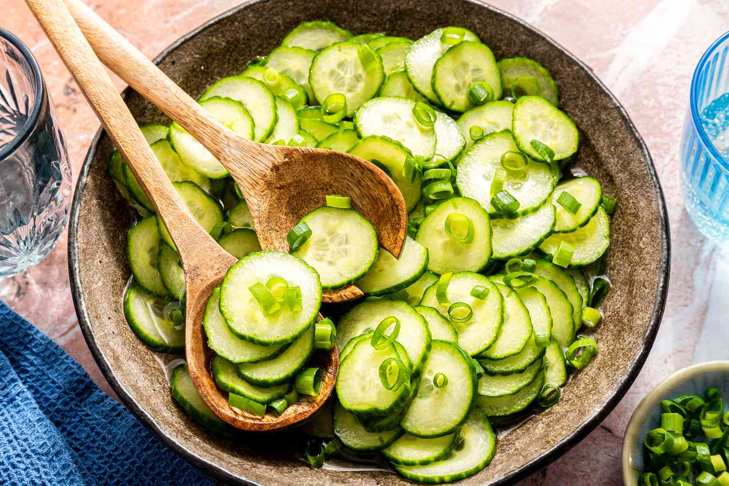 Bowl of sliced cucumbers with green onions and wooden spoons