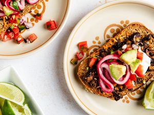 Black bean toast on a plate next to another plate with a serving and a bowl of lime slices