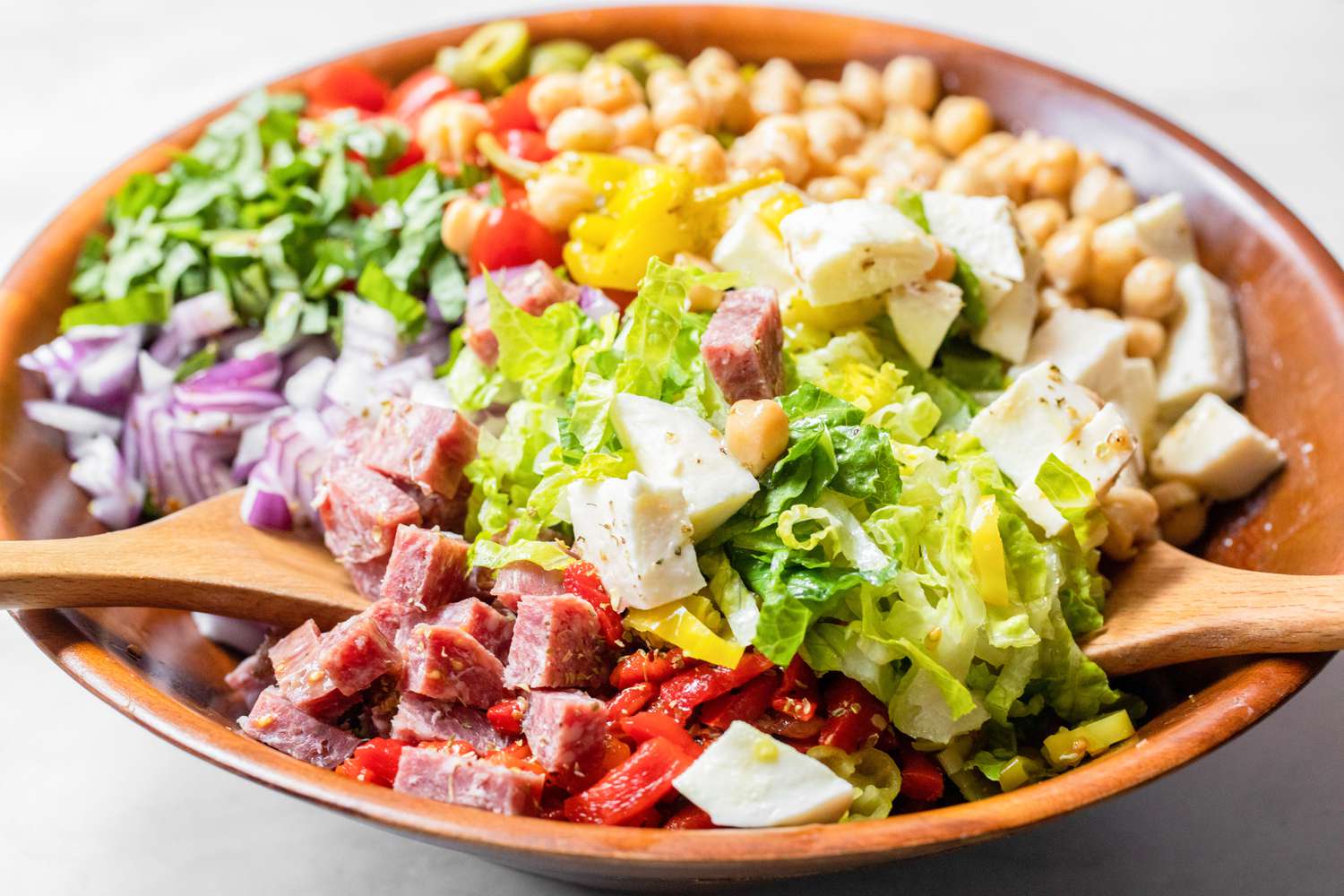 Two Serving Spoons Mixing a Bowl of Italian Chopped Salad 