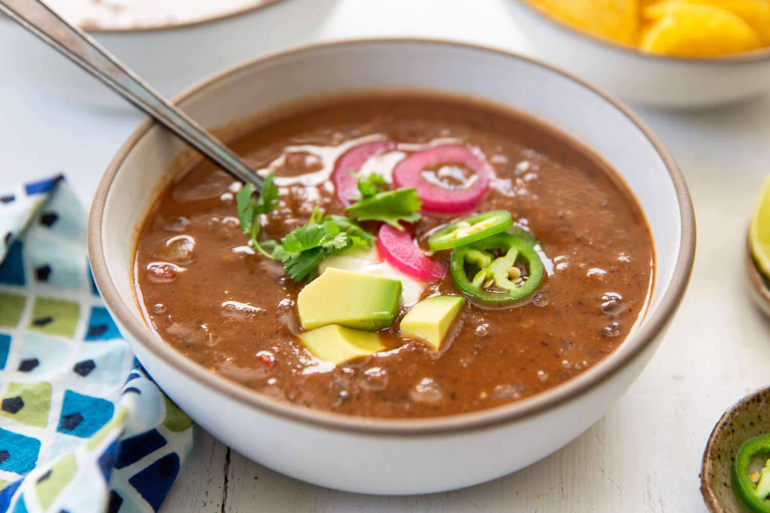 A bowl of 15-minute black bean soup, topped with avocado cubes, jalapeño slices, pickled onion and and cilantro