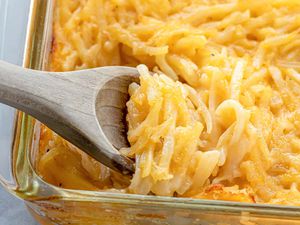 A close up side view of a glass casserole dish with a wooden spoon scooping out the potato casserole.