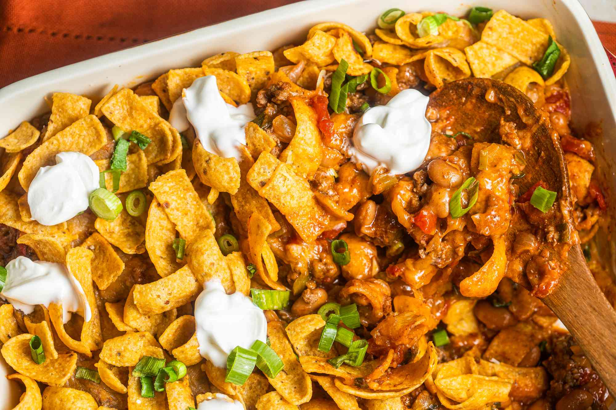 Walking taco casserole with dollops of sour cream in a casserole dish with a serving spoon (casserole dish missing some casserole)