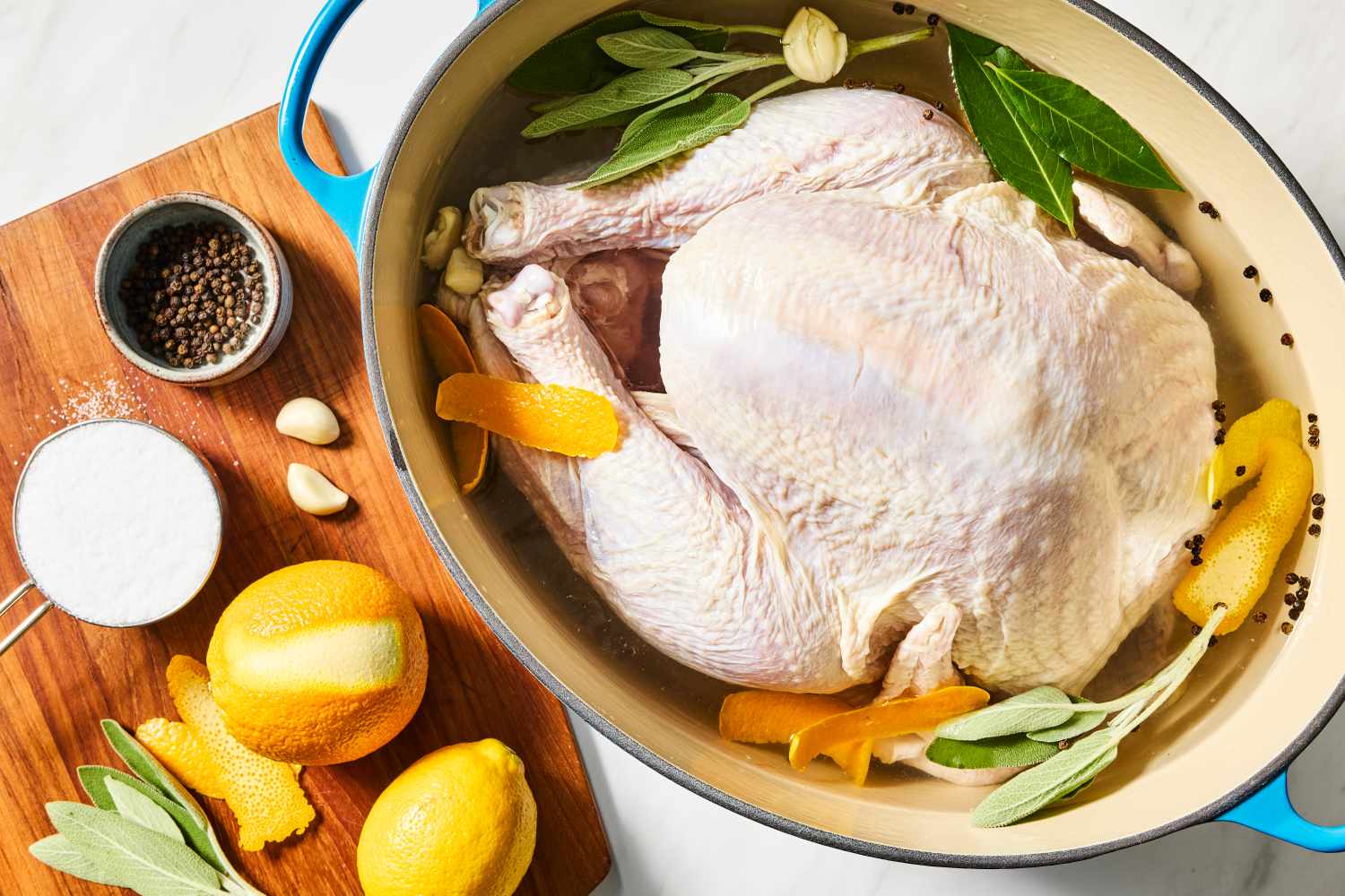 Raw turkey in a pot with herbs, citrus slices, spices, and brine, with ingredients for a brine on the side