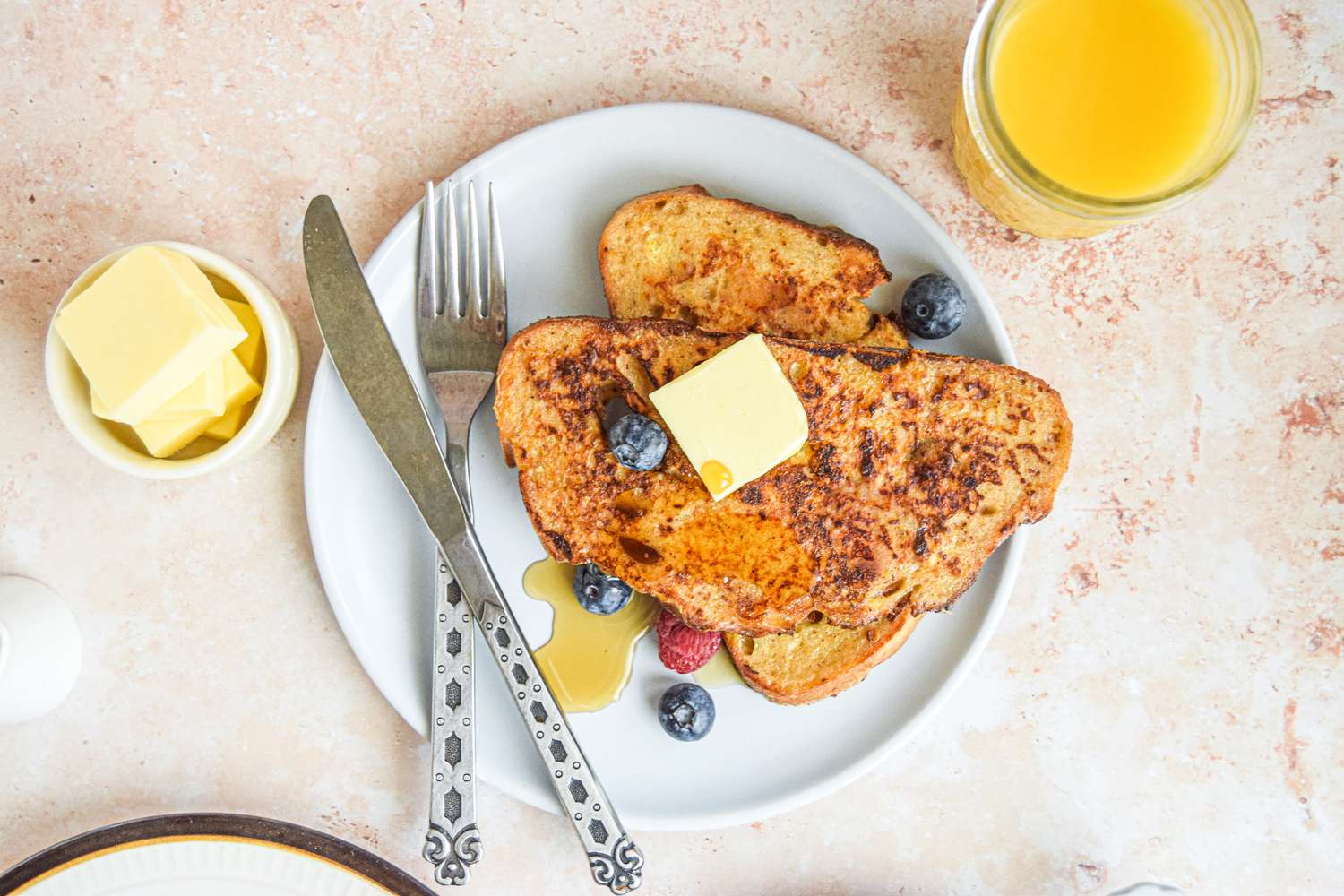 Easy French Toast on a Plate with Butter, Maple Syrup, and Berries, Surrounded by Glass of Juice and Small Bowl of Butter