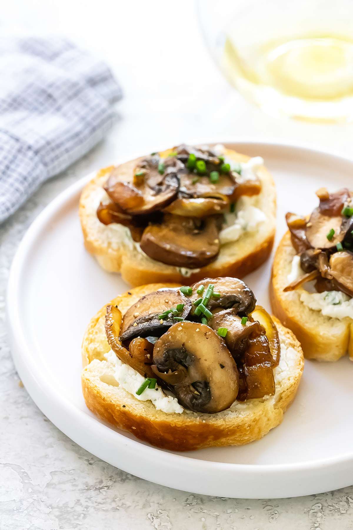 Three crostini topped with savory mushrooms and caramelized onions on a white plate.