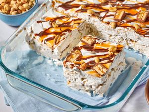 A dessert in a glass baking dish, topped with peanuts, caramel, chocolate drizzle, and candy pieces