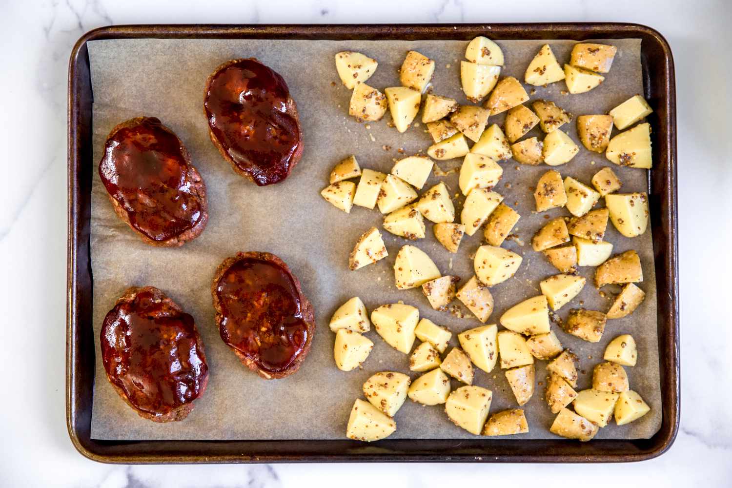 Mini meatloaves and chopped potatoes on a sheet pan.