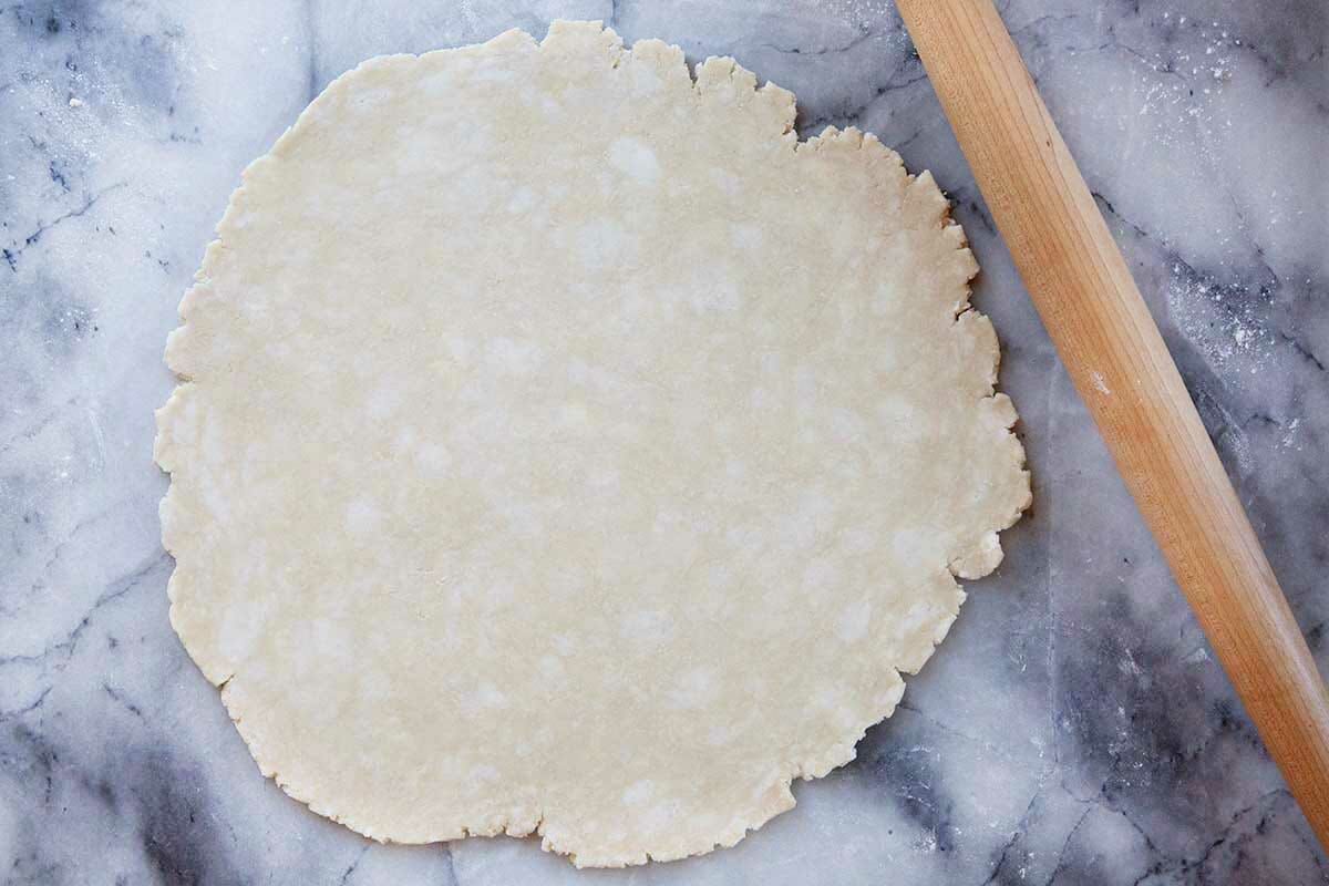 Shoo fly pie crust rolled out on a marble background with a rolling pin to the right.