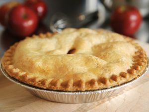 A storebought apple pie on a wooden surface with apples in the background