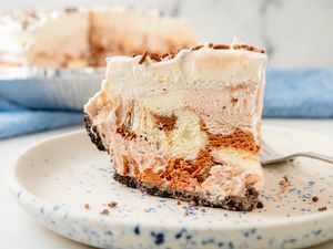 A slice of layered ice cream pie on a speckled plate with a fork