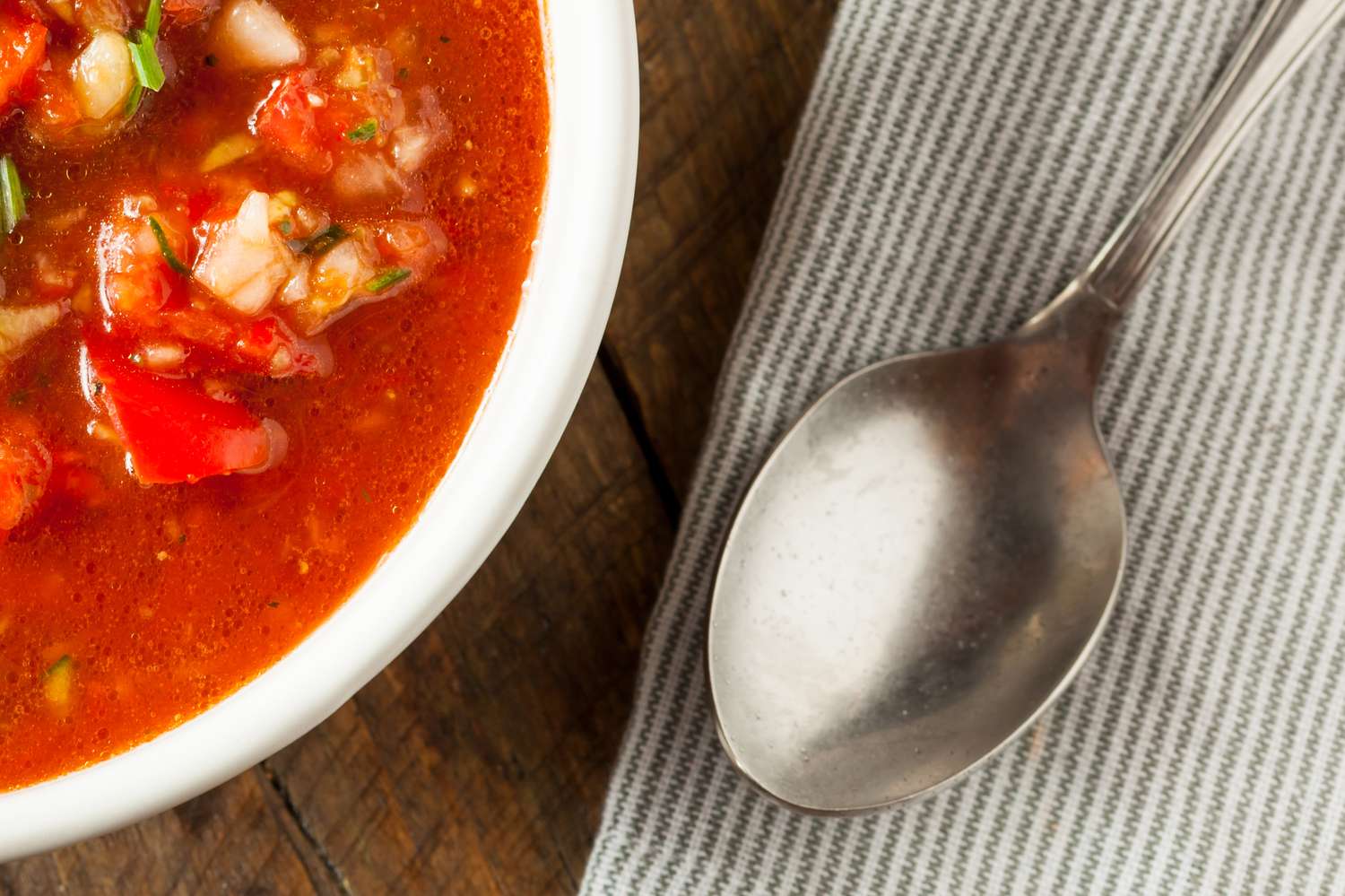 A bowl of soup next to a spoon on a striped napkin
