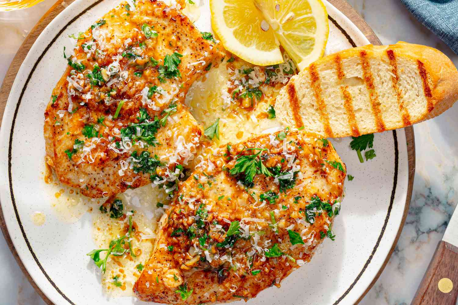 Overhead view of a plate chicken breasts of Garlic Knot Chicken recipe along with lemon slices and a piece of toasted bread
