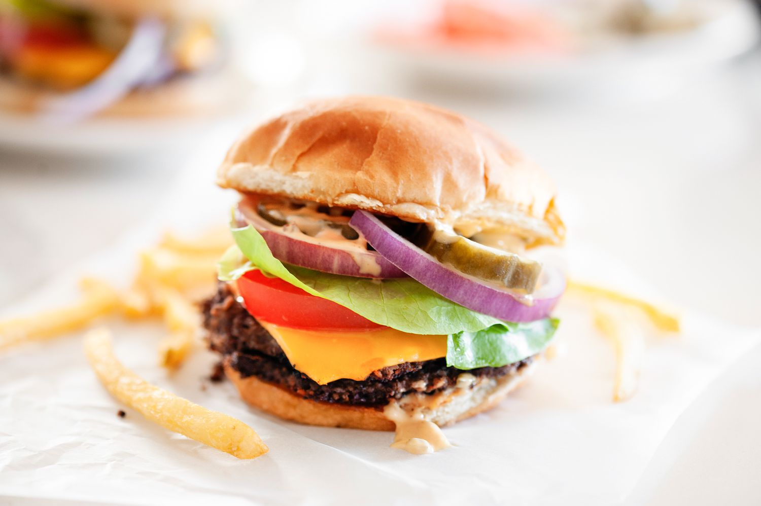 Black Bean Smash Burger on a Piece of Parchment Paper with French Fries, and in the Background