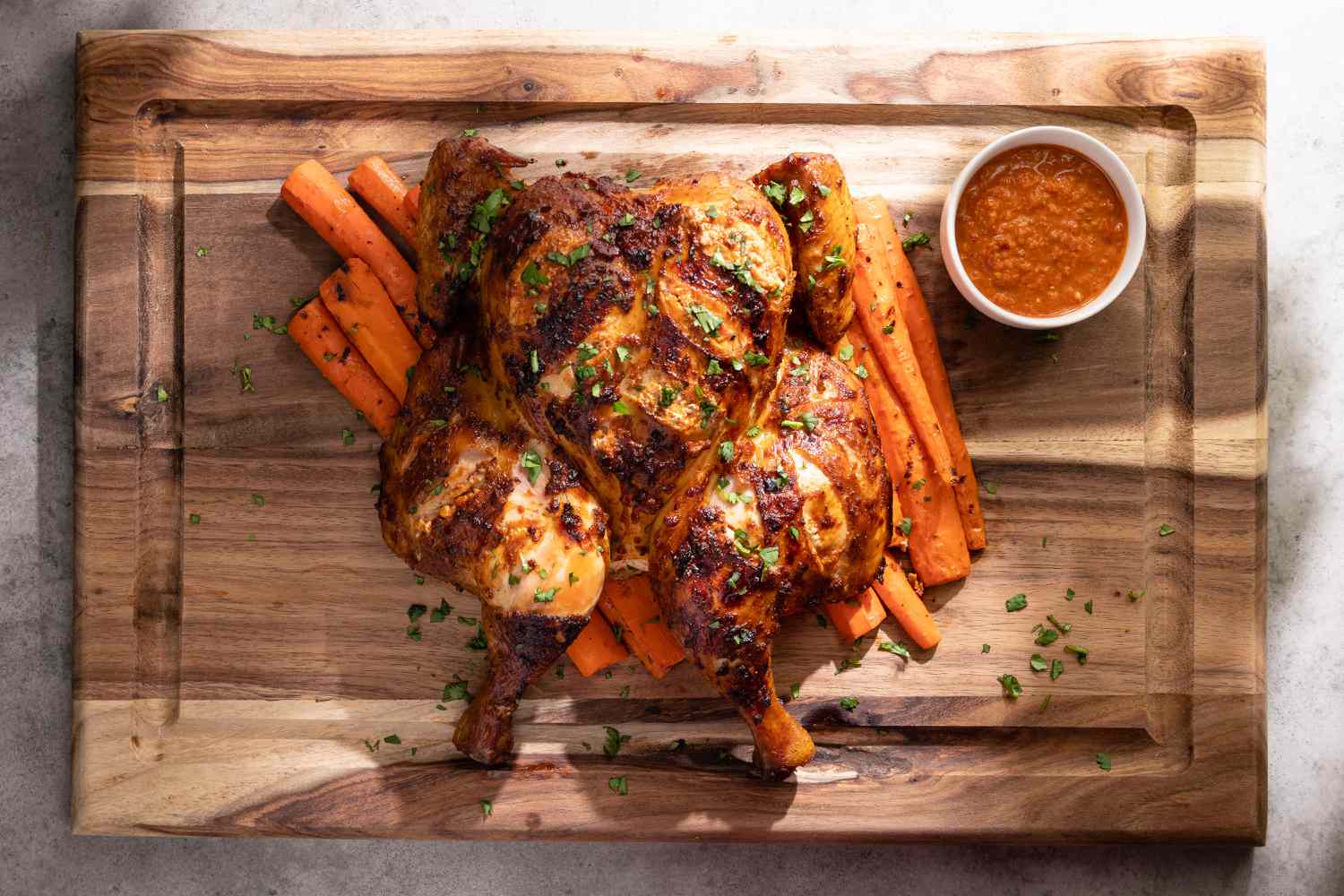 Smoked Spatchcock Chicken with Harissa Butter and Grilled Carrots on Cutting Board Next to Bowl of Harissa