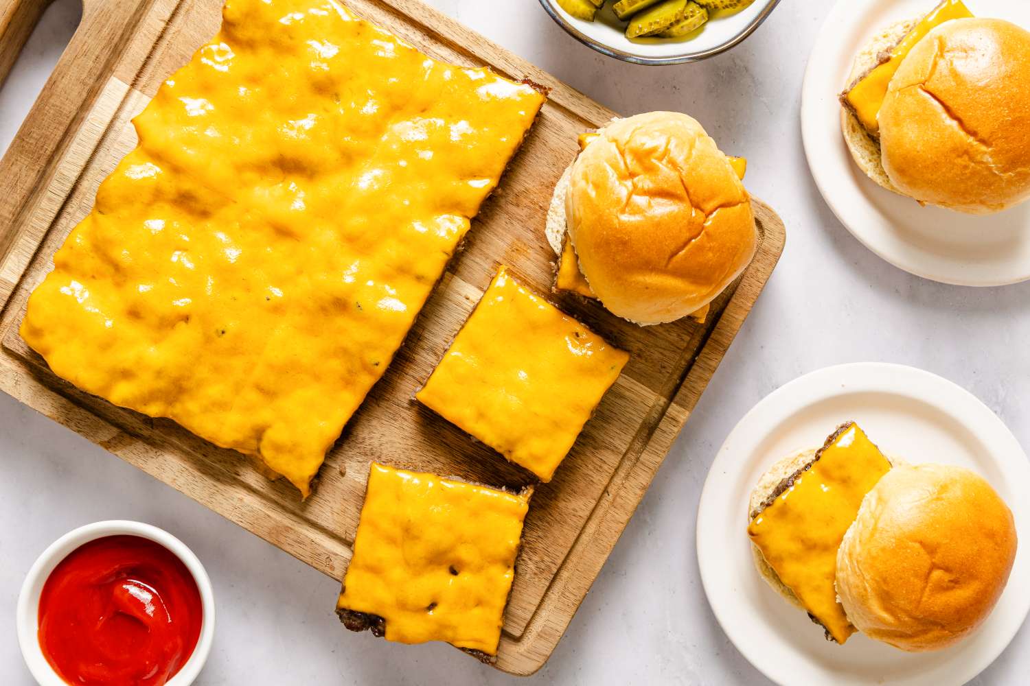Tray of cheeseburger sliders and buns with small dishes of pickles and ketchup