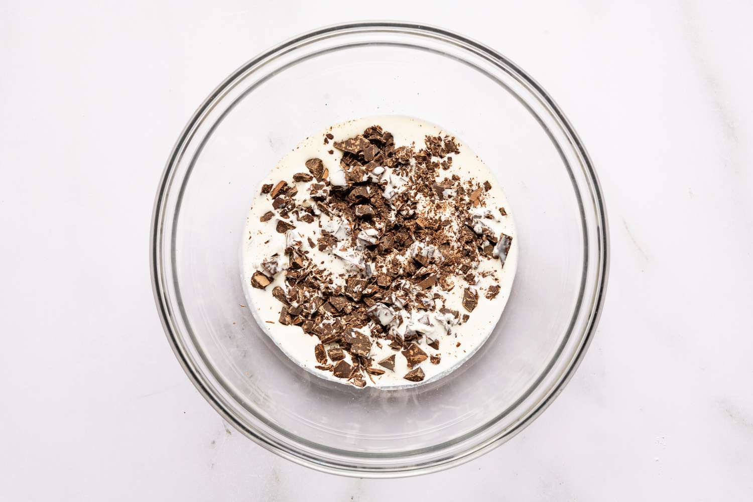 Overhead view of a clear glass bowl with cream and chocolate chunks for Easy Brooklyn Blackout Cake recipe