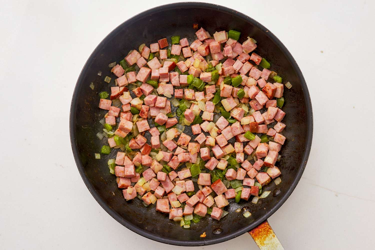 Ham cubes and bell pepper cubes cooked together in a pan for Denver omelette hashbrown casserole recipe