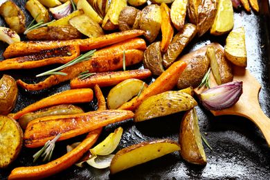 Roasted vegetables including carrots potatoes and onions on a baking tray garnished with rosemary