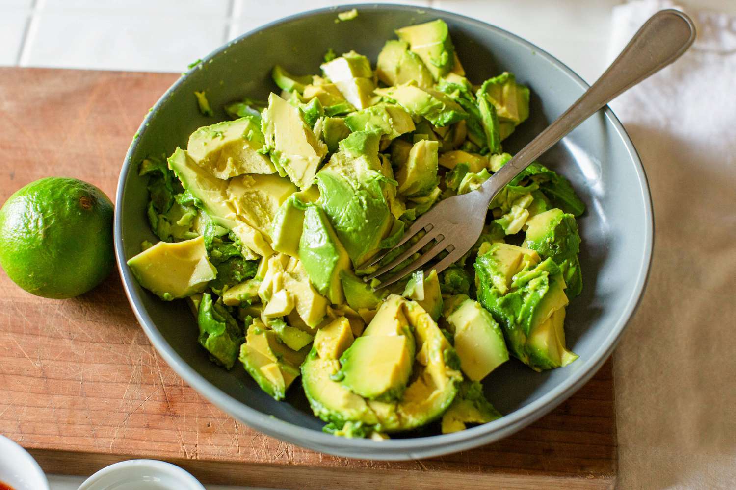 Chunked-up avocado in a shallow bowl with a fork; a lime sits to the side