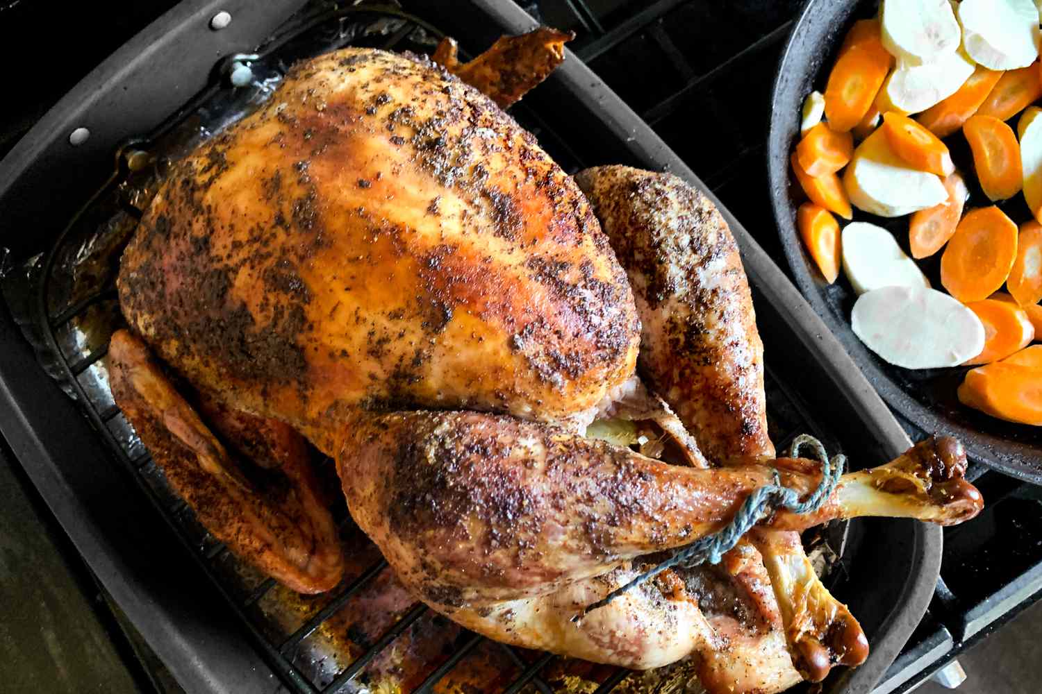 roasted turkey in a roasting pan with root veggies on the side