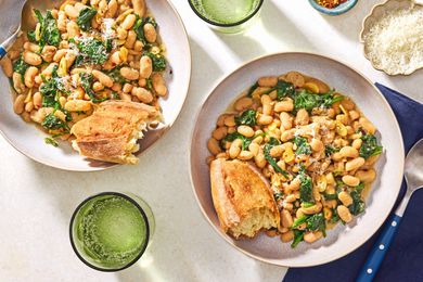 Overhead view of a bowl of 10-Minute Beans and Greens with a chunk of bread all next to a spoon and resting on a blue cloth napkin