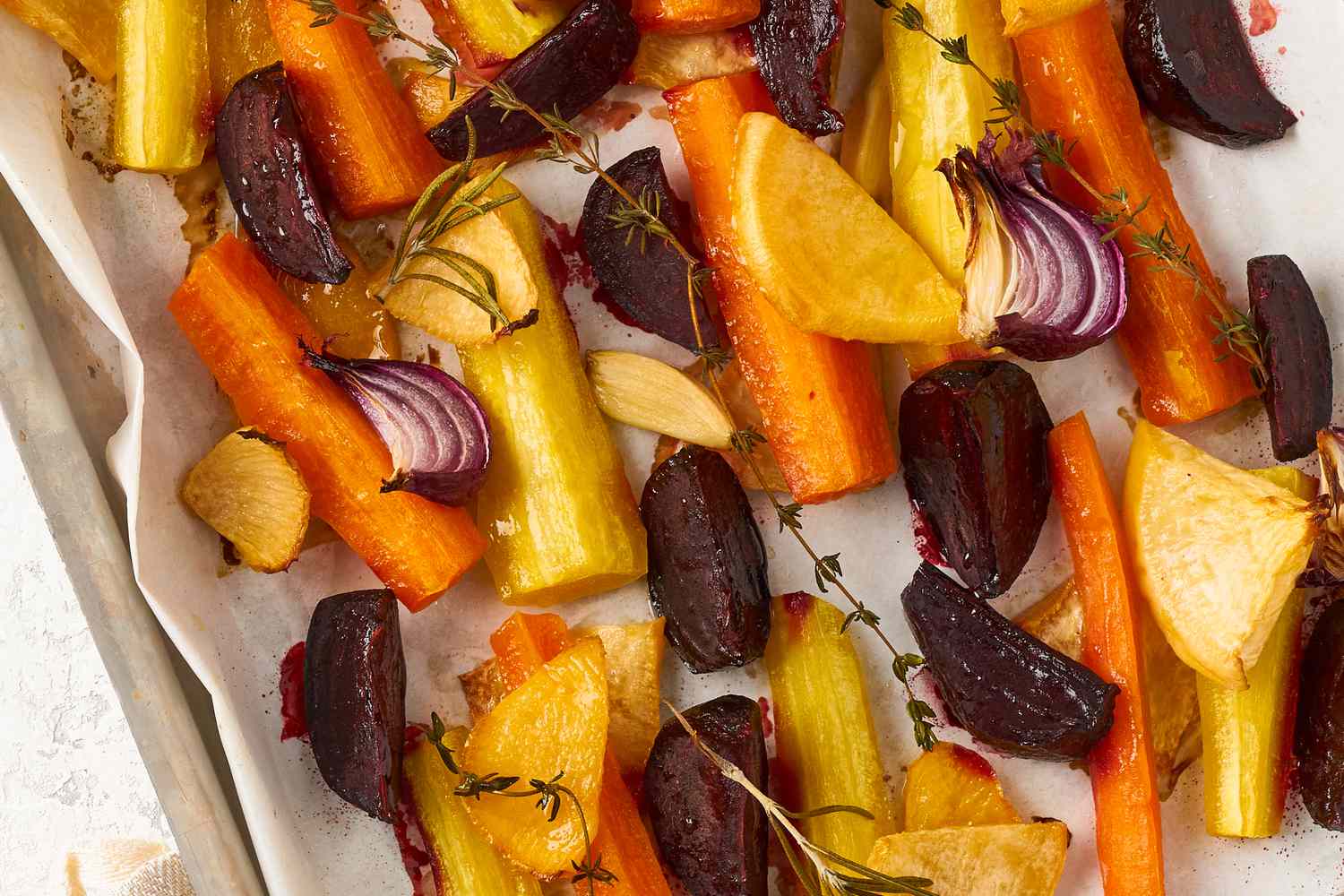 Roasted carrots, shallots, garlic, and beets on a parchment-lined sheet pan