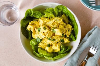 Curry chicken salad served on lettuce leaves in a bowl with forks and a napkin nearby
