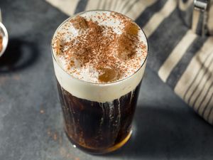 A glass of German iced coffee with whipped cream and cocoa powder on a dark surface